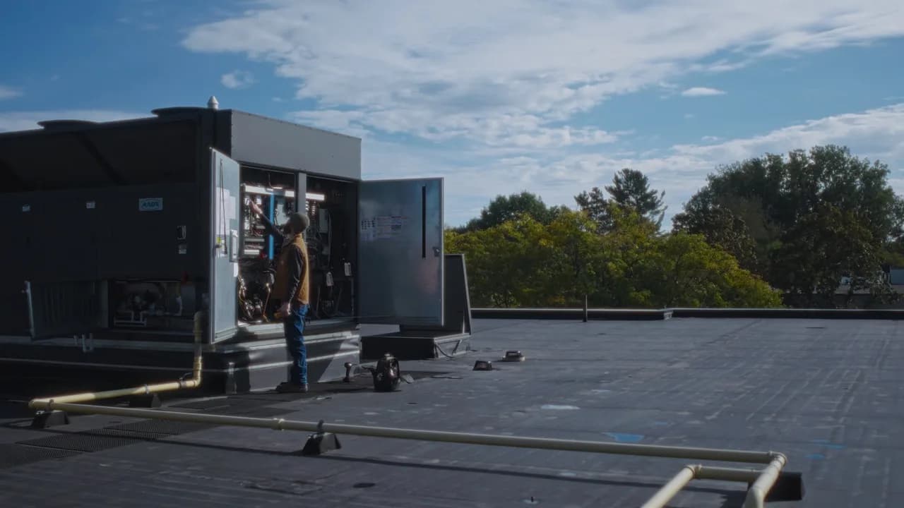 Grand Valley Automation technician services rooftop controls equipment under an open sky.